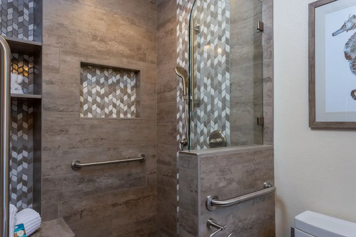 “Bathroom remodel with horizontal shower niche and vertical multi-shelf niche featuring geometric accent tile and grab bars.”