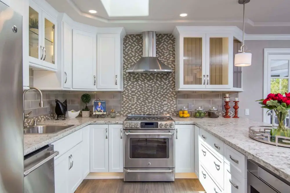 "U-shaped kitchen with mosaic tile backsplash, stainless steel range hood, white shaker cabinets, and granite countertops for efficient cooking and prep zones."