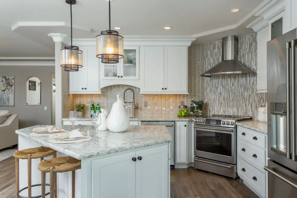 Bright transitional kitchen with a marble-top island, glass pendants, and white cabinetry accented by a mosaic tile backsplash and stainless steel range.