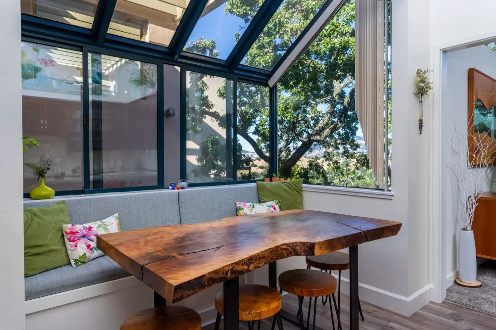 ozy breakfast nook with floor-to-ceiling windows and a live-edge wood table surrounded by modern stools, bringing in natural light and outdoor views.