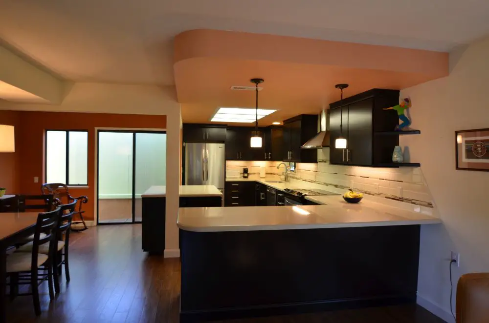 Contemporary Rossmoor kitchen remodel with sleek black cabinetry, quartz countertops, pendant lighting, and a peninsula that opens to the dining area — designed by Toupin Construction.