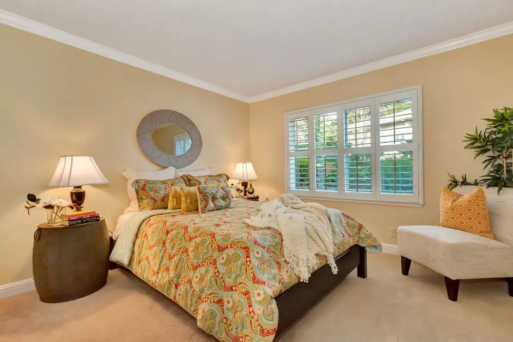 Cozy bedroom remodel in Walnut Creek featuring soft beige walls, white trim, plantation shutters, and colorful bedding — designed by Toupin Construction for a warm, inviting retreat.