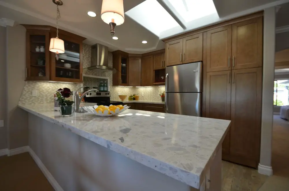 Finished kitchen remodel featuring warm wood cabinets, quartz countertops, stainless steel appliances, under-cabinet lighting, and a large peninsula with skylight overhead.