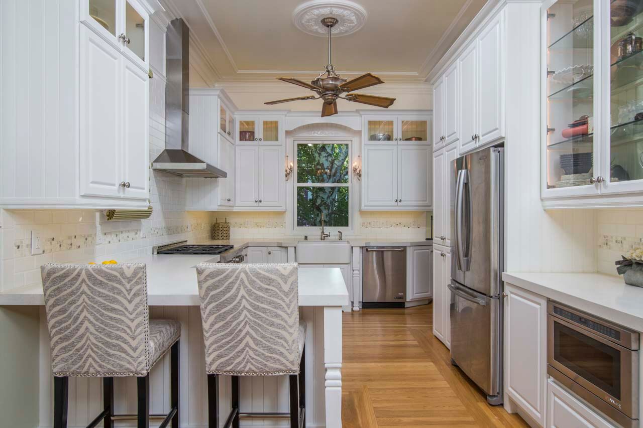 White shaker kitchen with quartz countertops, stainless steel appliances, farmhouse sink, and breakfast bar seating.