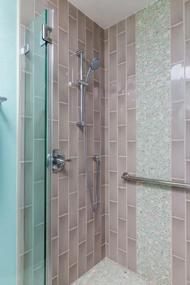 “Modern Rossmoor walk-in shower featuring taupe vertical subway tiles with a mint green pebble accent strip and chrome handheld shower fixture.”