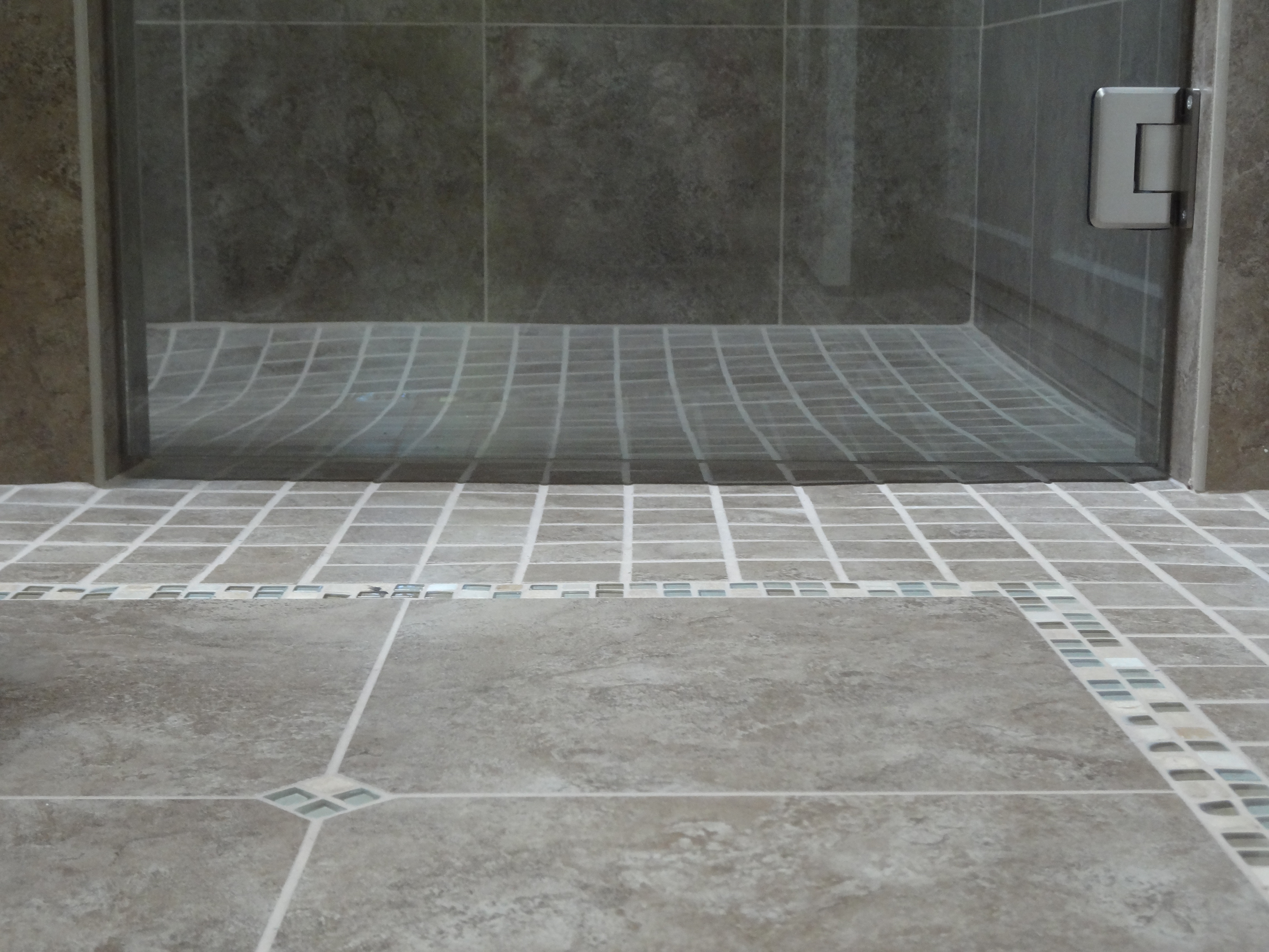 “Close-up of no-threshold shower entry with seamless tile transition from bathroom floor to shower.”