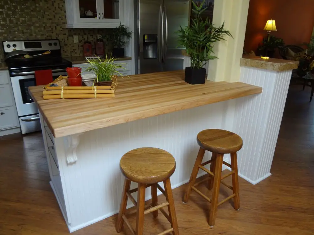 Small kitchen peninsula with light butcher block countertop, white beadboard paneling, and two wooden stools.