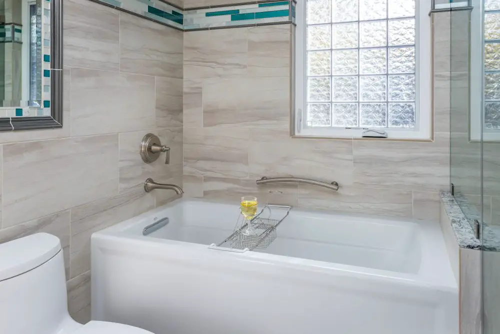 Modern bathroom remodel in Rossmoor featuring a white soaking tub with brushed nickel grab bars, large-format beige wall tile, and teal accent border tile.