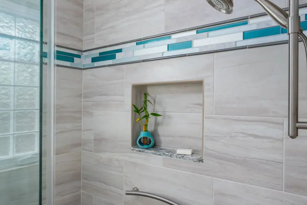Curbless shower with light gray porcelain tile, blue glass accent band, and built-in niche featuring a teal vase — modern and accessible East Bay bathroom design.