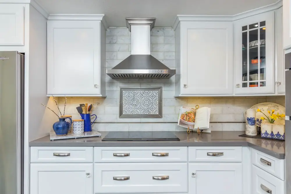 “Classic white East Bay kitchen with marble-look subway tile backsplash, stainless steel hood, and decorative patterned tile inset above the cooktop.”