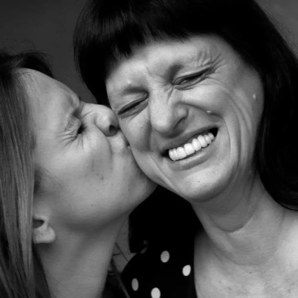 Daughter kissing her mother on the cheek in a black-and-white family portrait.