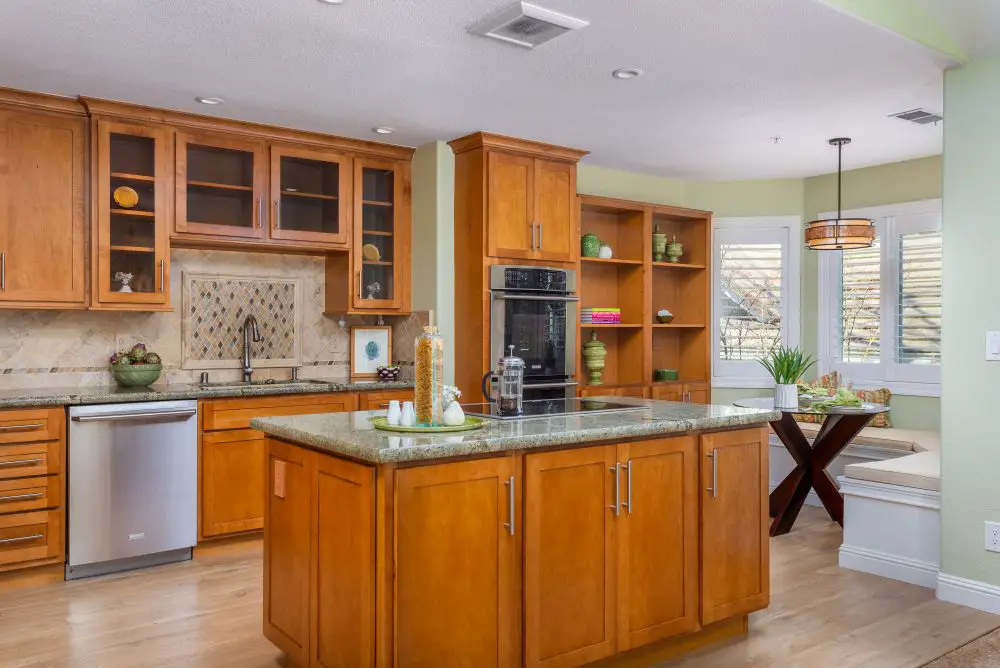 Warm traditional kitchen with honey-colored cabinets, a central island, granite countertops, and built-in shelving near a breakfast nook.