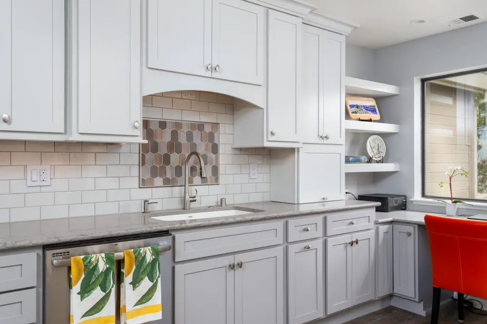 White shaker cabinets with arched cabinet detail over tile backsplash insert in a gray kitchen