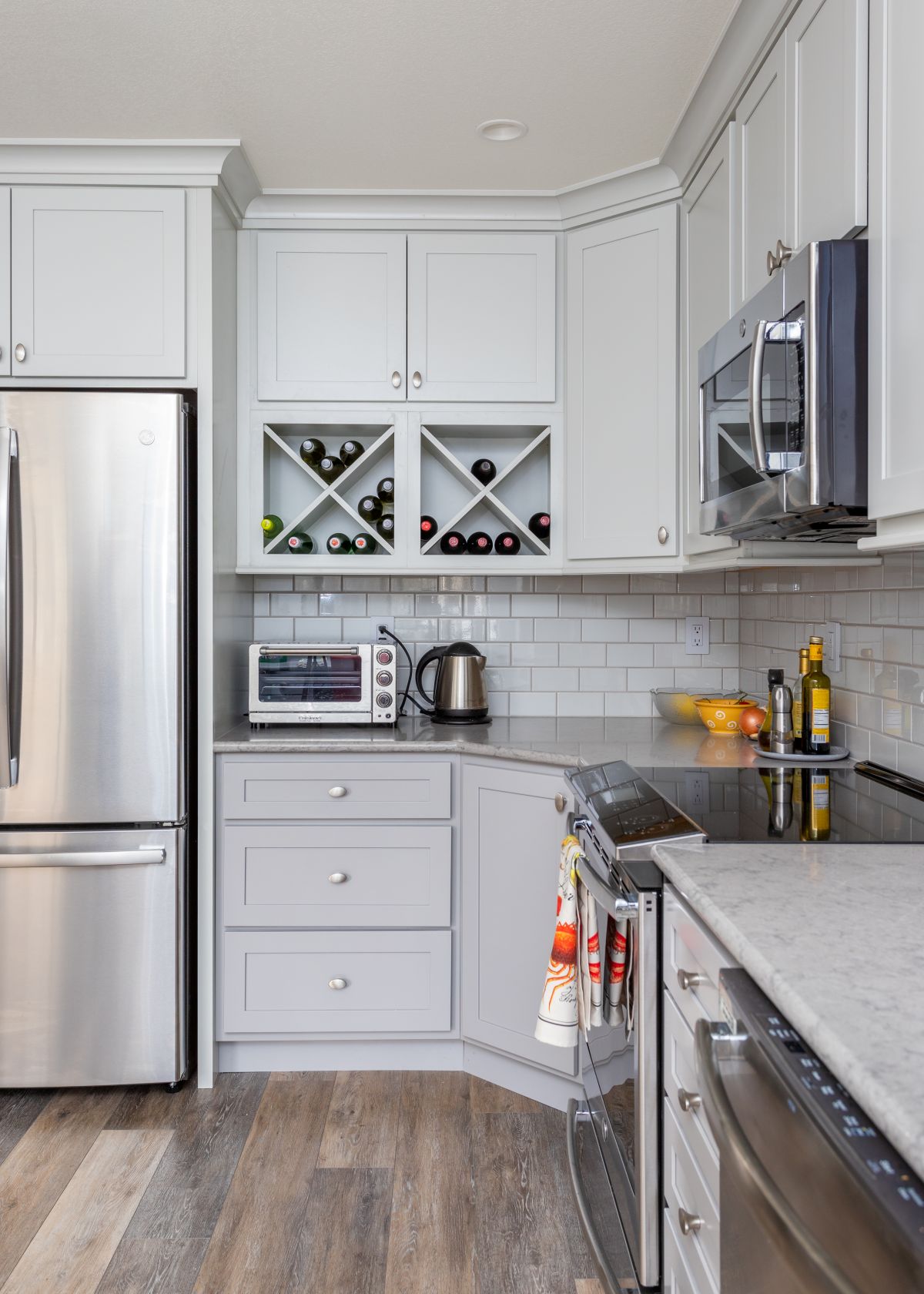 Bright kitchen with light gray cabinetry, stainless steel appliances, and glossy white subway tile backsplash. Features a built-in wine rack, marble-look counters, and wood-look flooring.