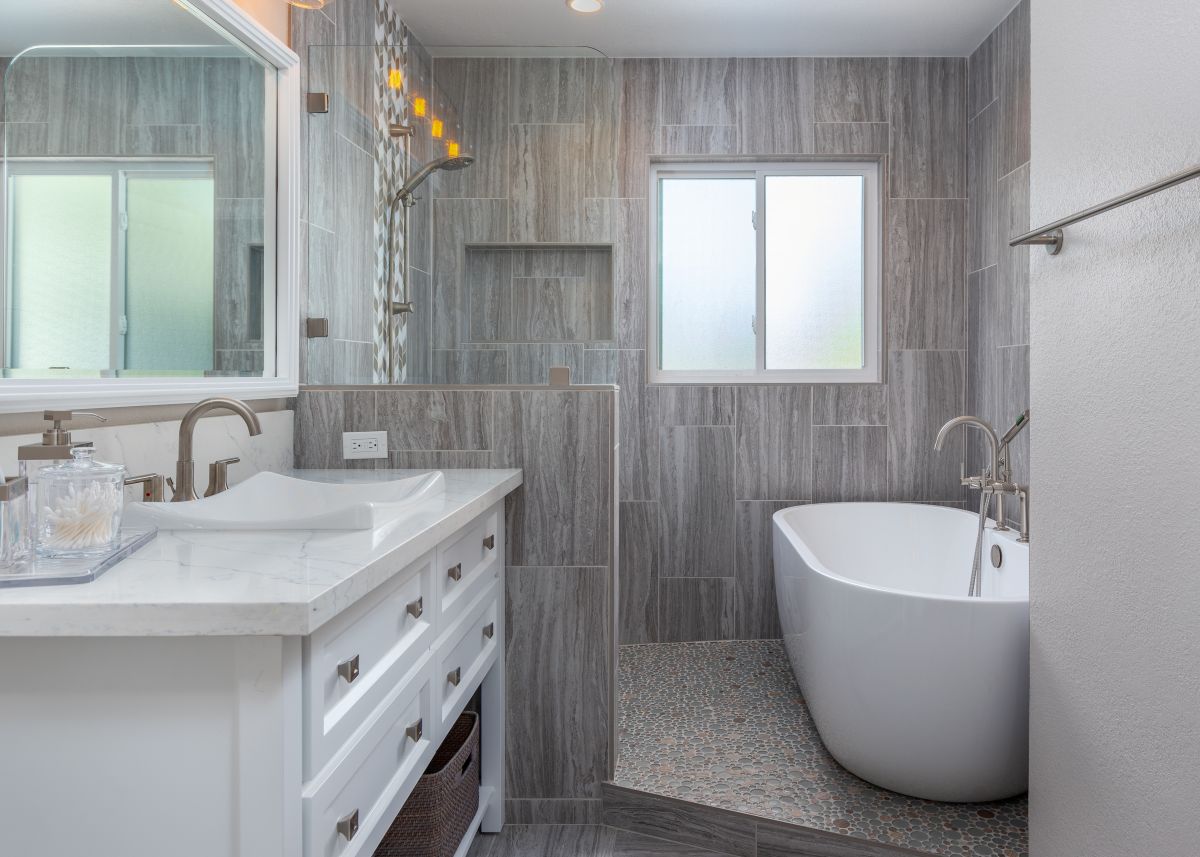 “No-threshold shower with gray tile walls, seamless entry, and freestanding soaking tub in modern bathroom remodel.”