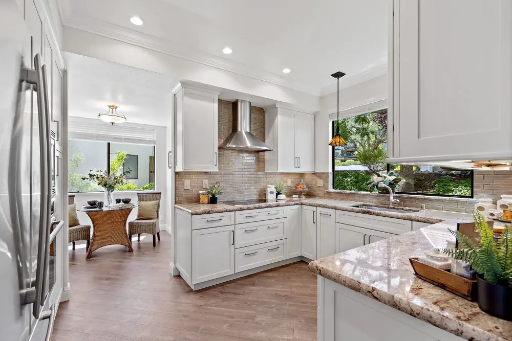Elegant East Bay kitchen renovation with white cabinetry, bronze tile backsplash, and natural light highlighting granite counters—by Toupin Construction.