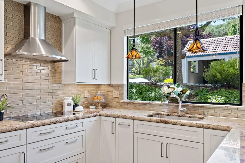 “Warm contemporary kitchen in Rossmoor with glossy beige subway tile backsplash, white shaker cabinets, and bronze pendant lighting over the sink.”