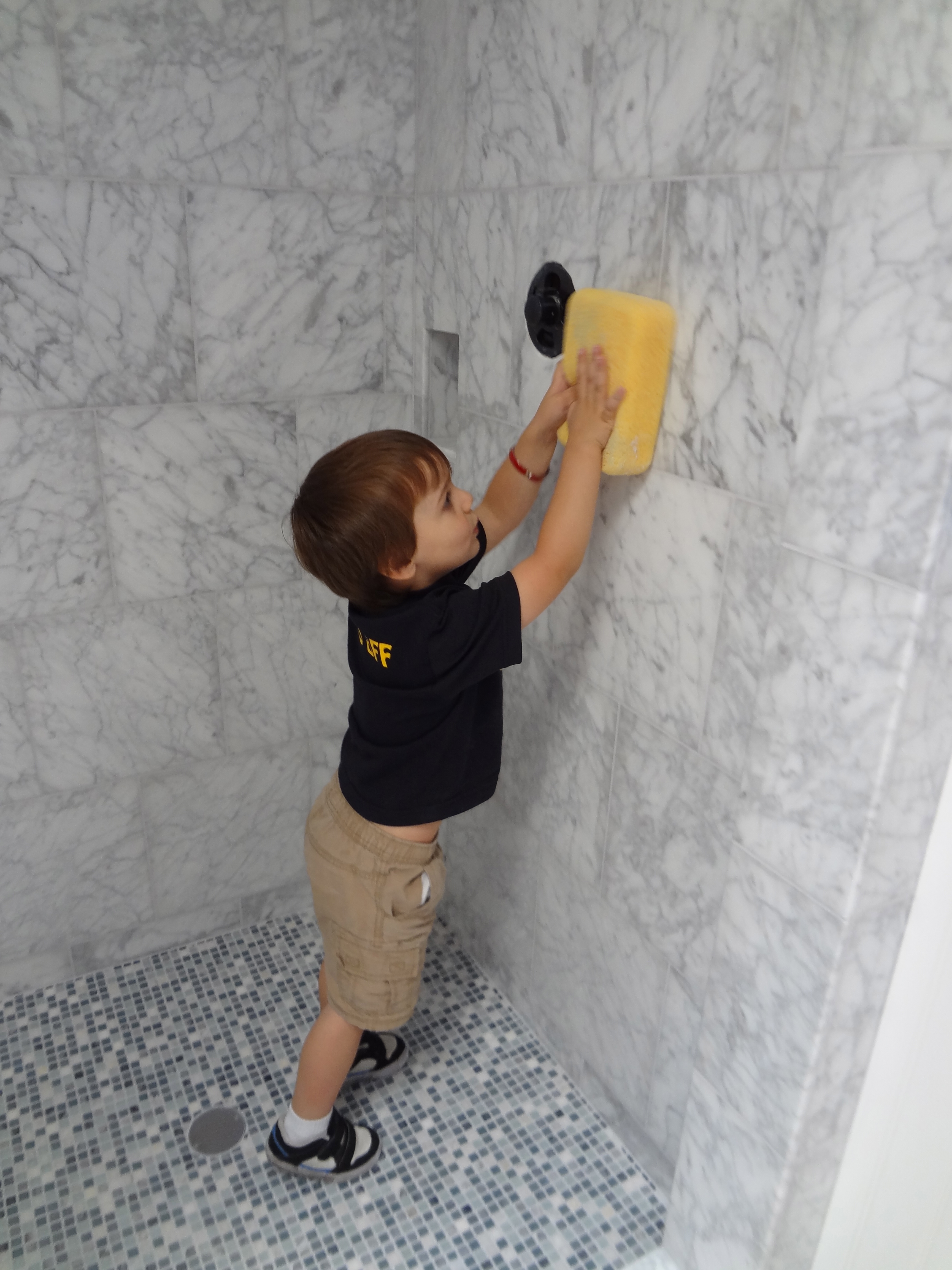 Toddler helping apply epoxy grout in marble shower with sponge during tile installation