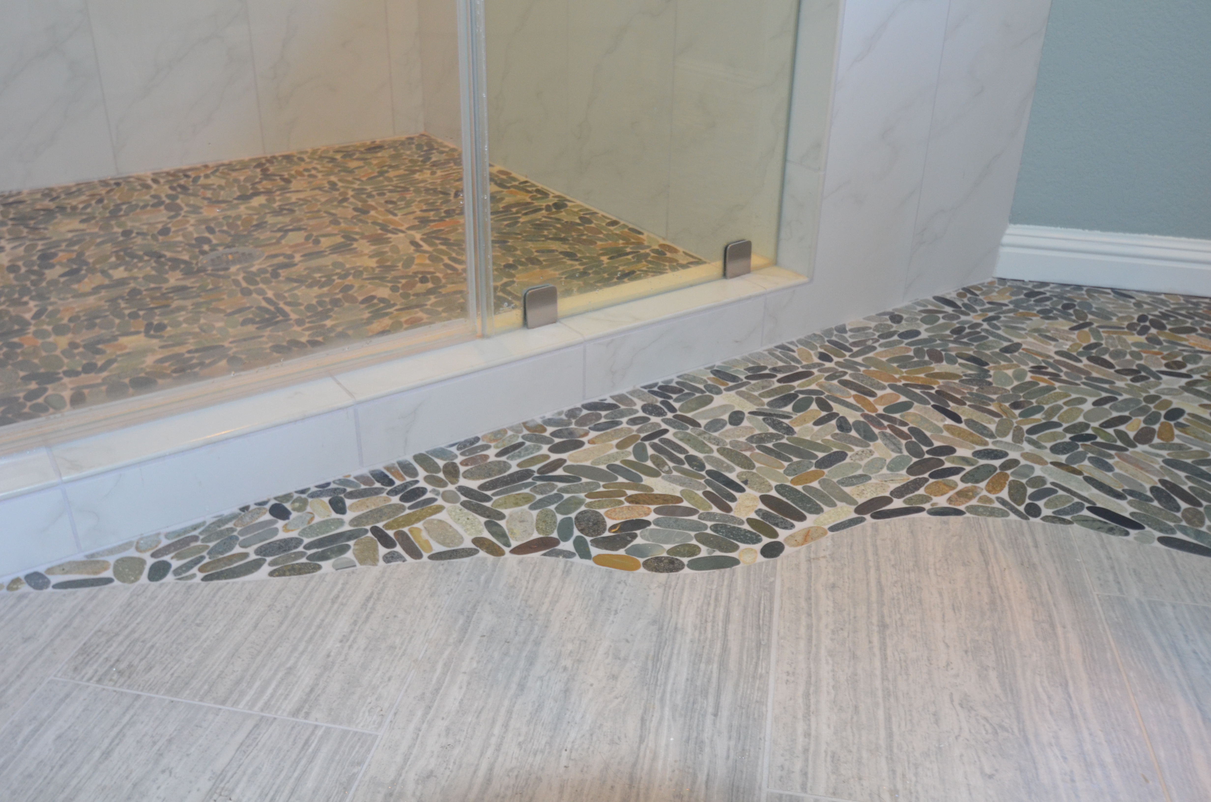 Pebble tile shower floor with curbless transition into bathroom flooring