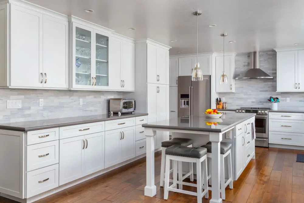"Spacious modern kitchen with large island, pendant lighting, and clear cooking and prep zones along white shaker cabinets and gray countertops."