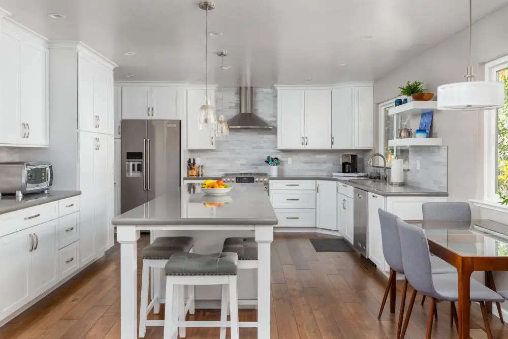 Spacious contemporary kitchen with a long quartz island, white cabinets, gray countertops, and pendant lights over hardwood floors.