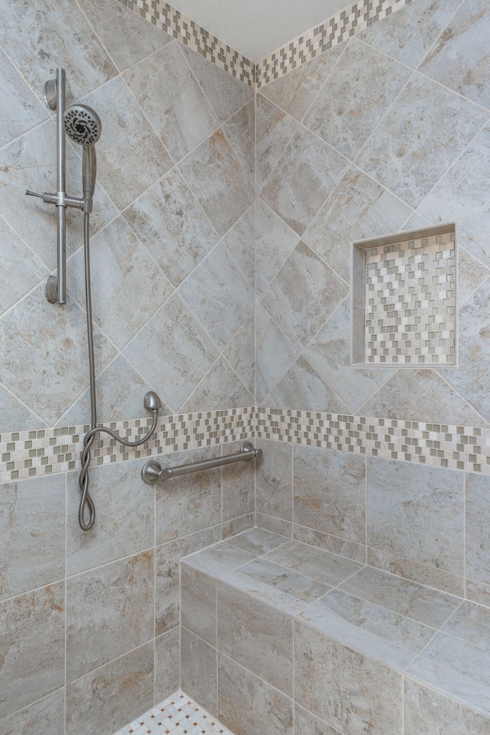 Stone-look tiled shower with built-in bench, grab bar, and mosaic trim — universal design blending safety, comfort, and classic style.