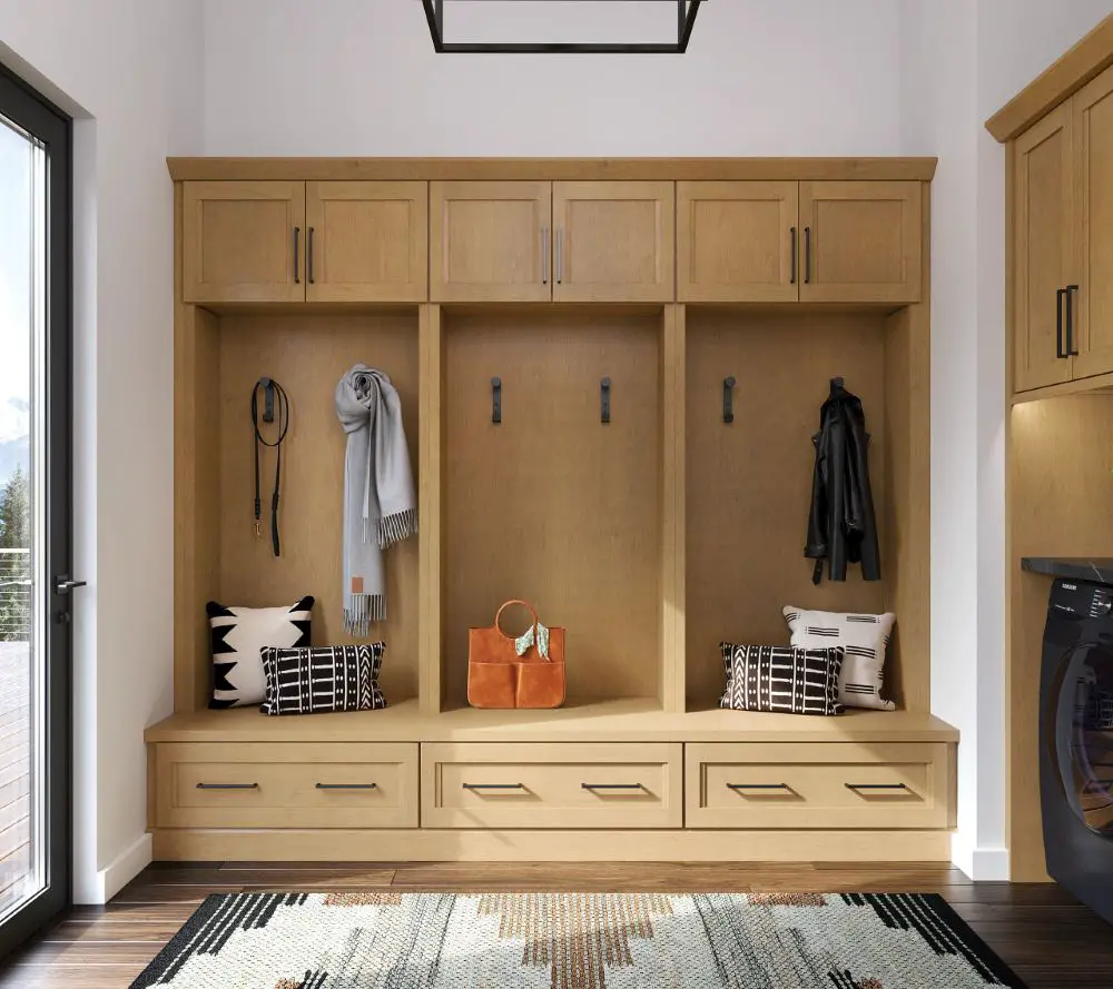 Warm natural wood KraftMaid mudroom cabinetry with built-in bench, upper storage cabinets, black metal hooks, and modern farmhouse styling by Toupin Construction.