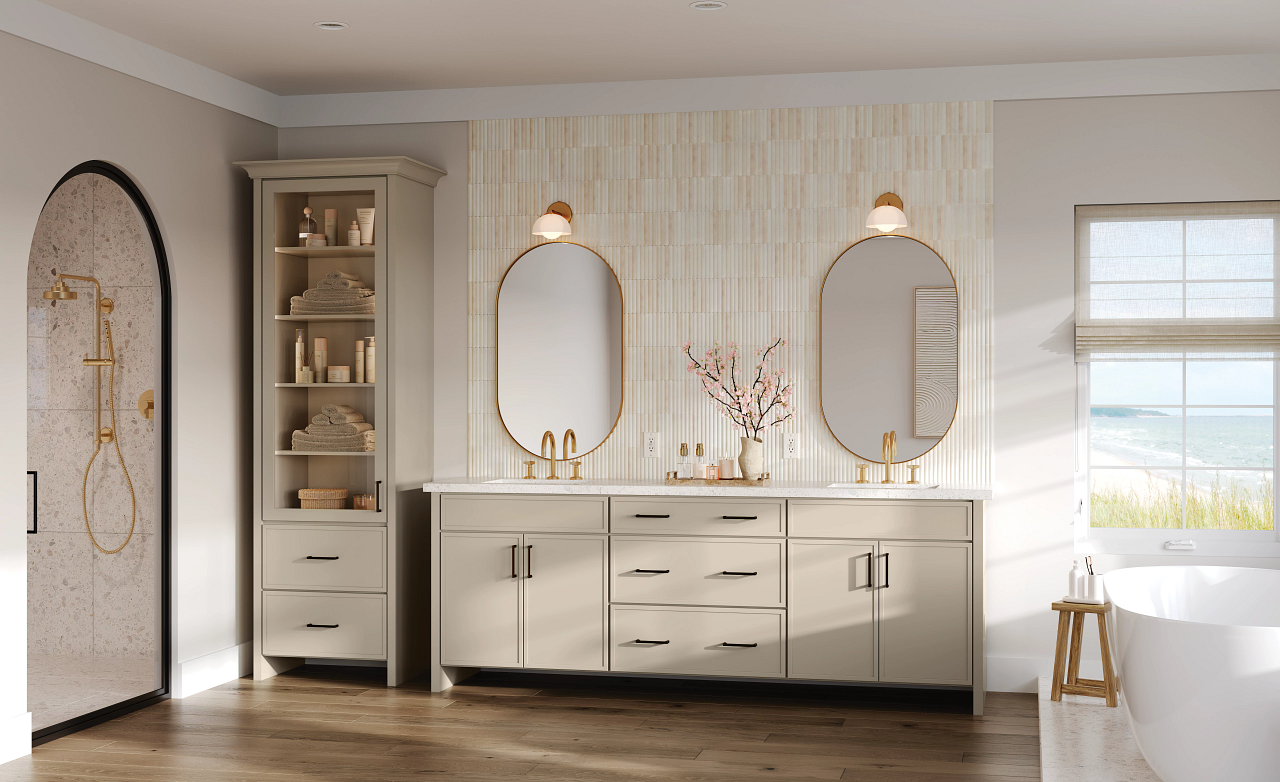 Elegant bathroom featuring KraftMaid Dorsey cabinetry in a soft neutral finish, paired with gold fixtures, oval mirrors, and a freestanding tub for a warm, coastal-inspired retreat.