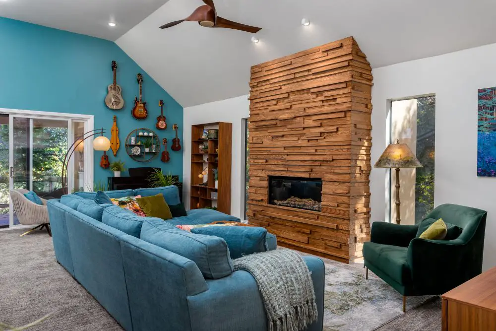 Teal accent wall with crisp white ceiling cut line in a vaulted living room, wood-slat fireplace surround