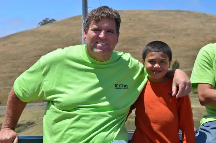 Tim Toupin sitting beside a young boy at an outdoor community event wearing a Toupin Construction shirt.