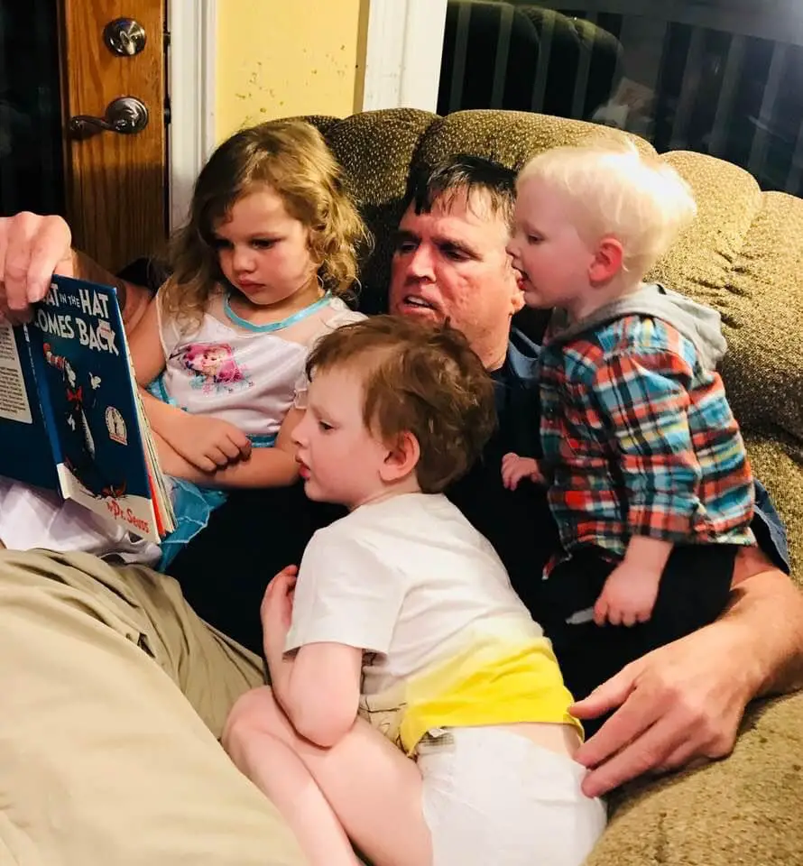 Tim Toupin reading a Dr. Seuss book to three young children while sitting together on a couch.