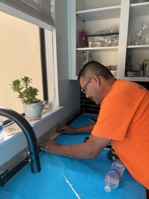 Adan installing black subway tile kitchen backsplash during a home remodel in Walnut Creek, CA, carefully measuring and setting tile beneath white shaker cabinets with countertops protected.