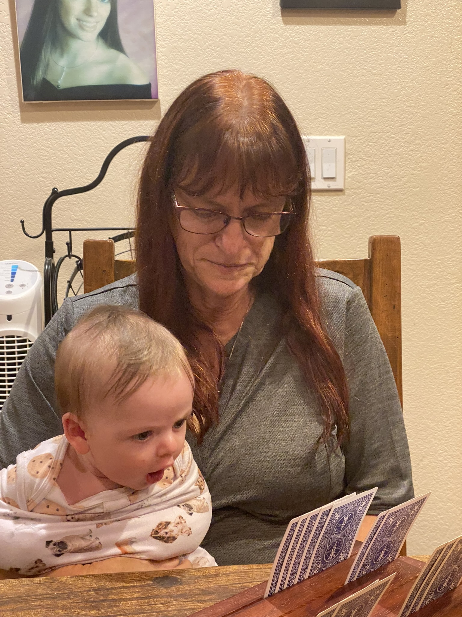 Grandmother holding a baby while sitting at a table during a family card game.