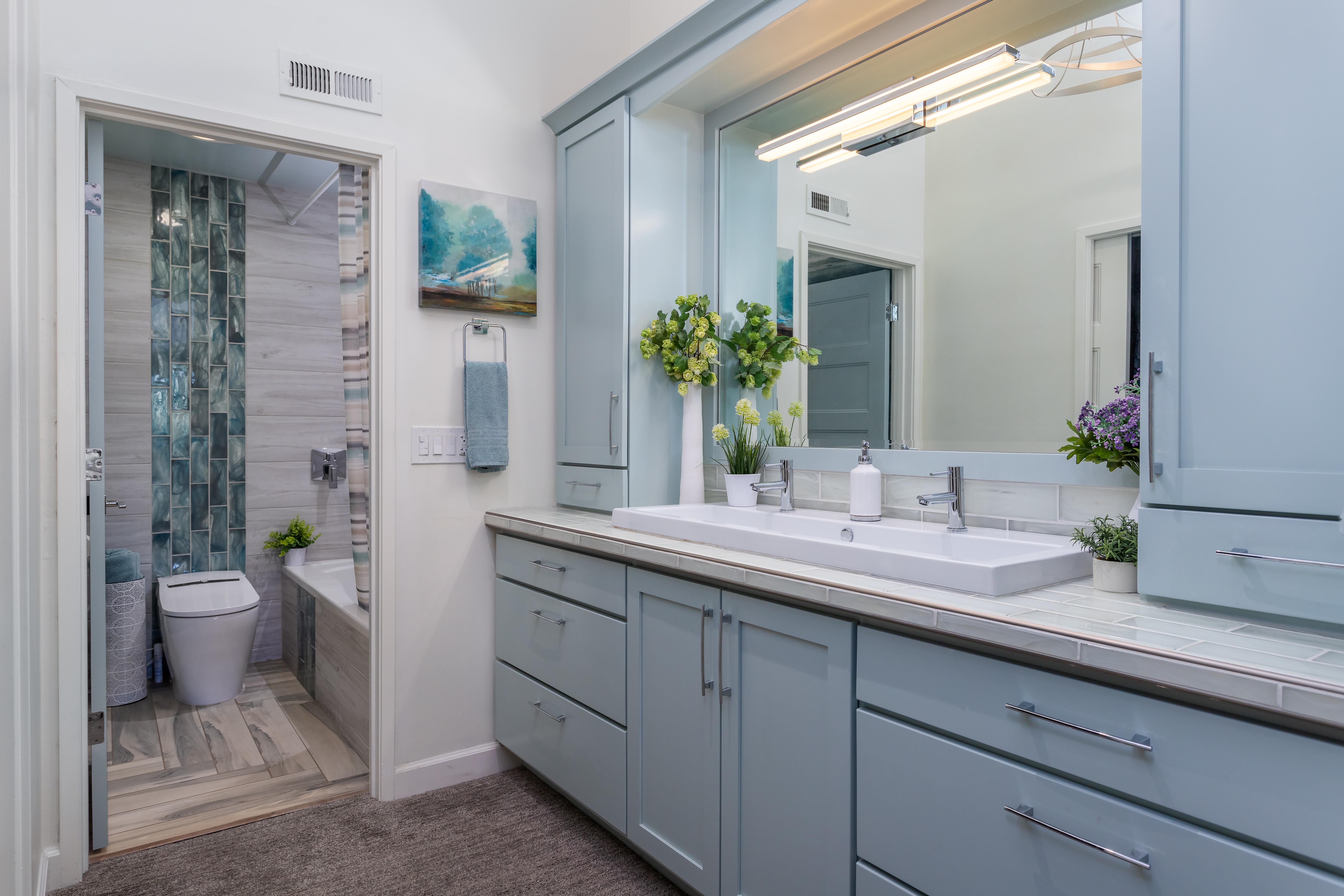 Modern bathroom with large wall mirror and light blue vanity with sleek hardware