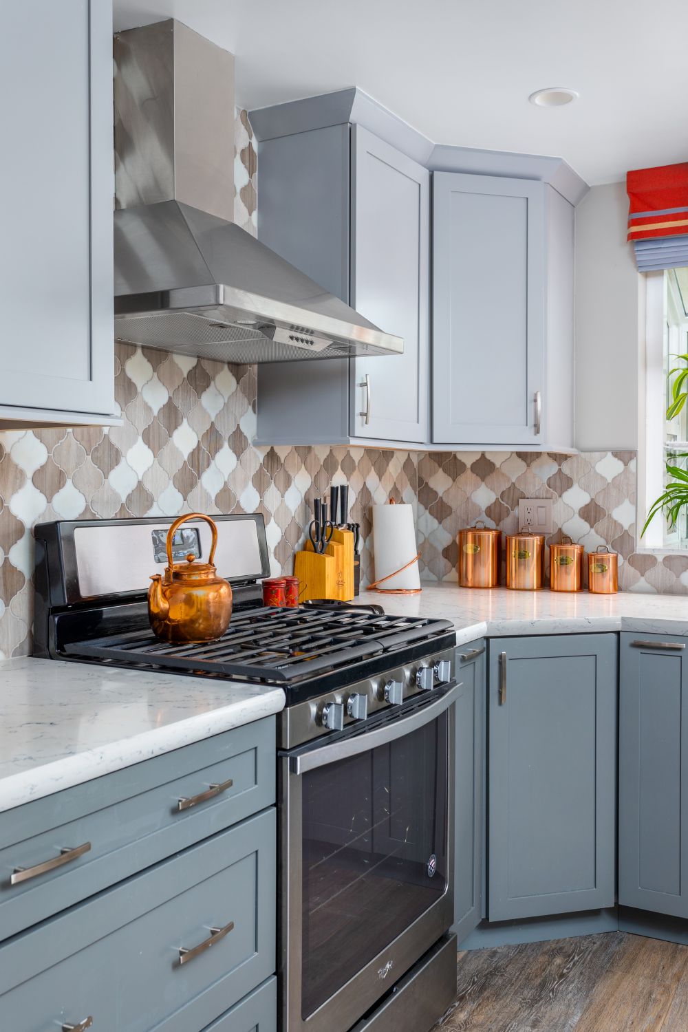 Blue gray kitchen cabinets with patterned tile backsplash and stainless steel range hood