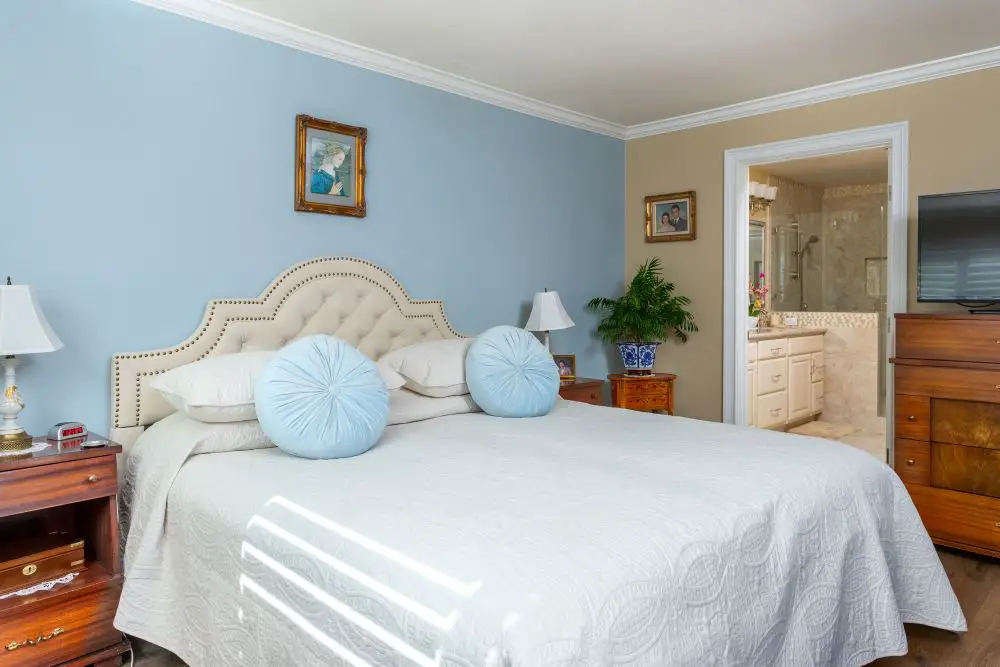 Bedroom with blue accent wall and beige wall showing cool and warm paint undertone comparison.