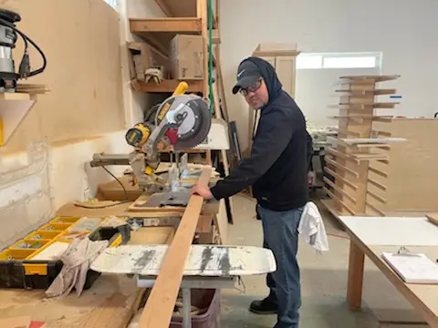 Worker cutting wood panels for cabinet refacing in workshop.
