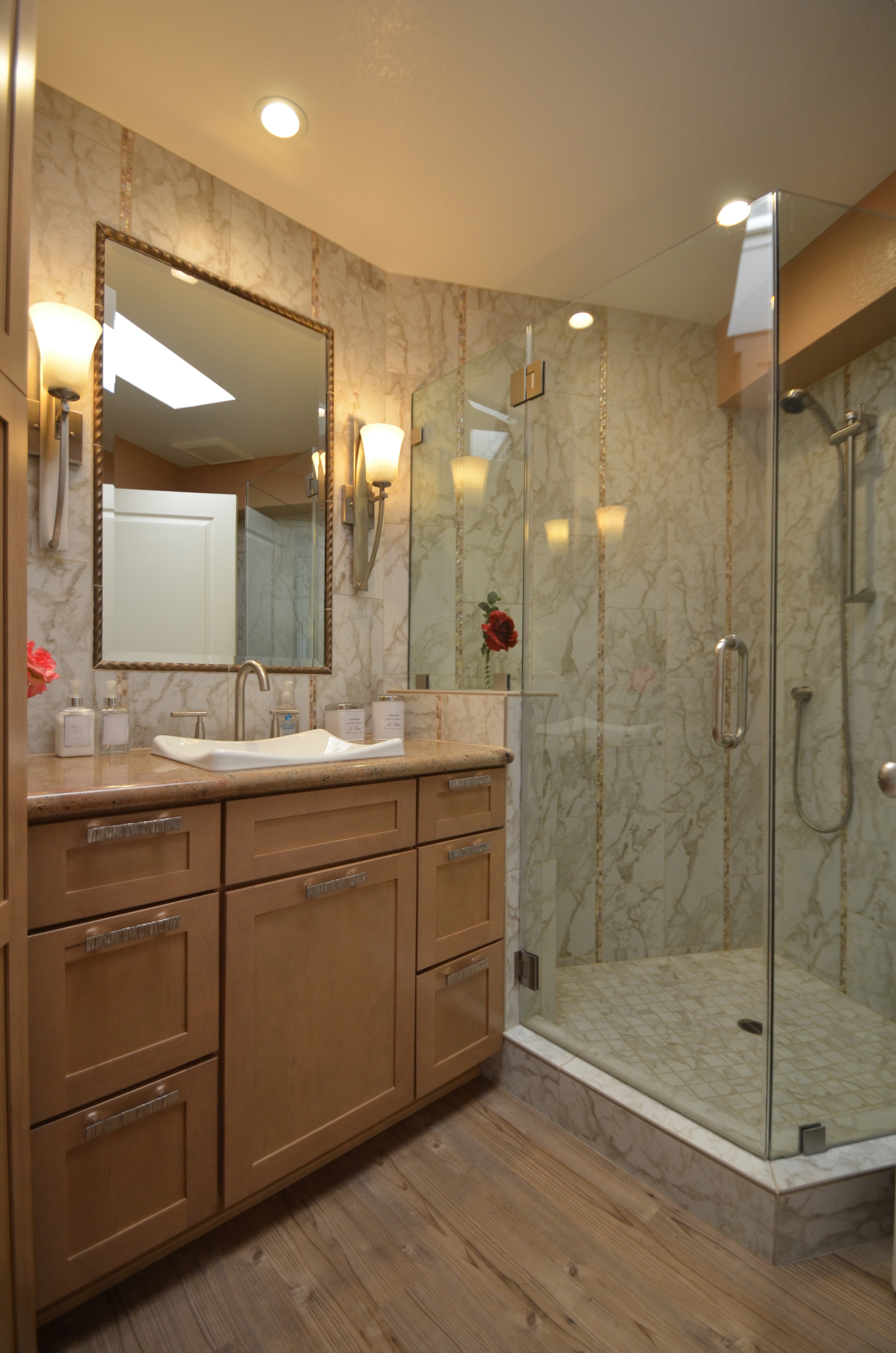 Custom marble tile shower with glass enclosure and wood vanity in bathroom remodel