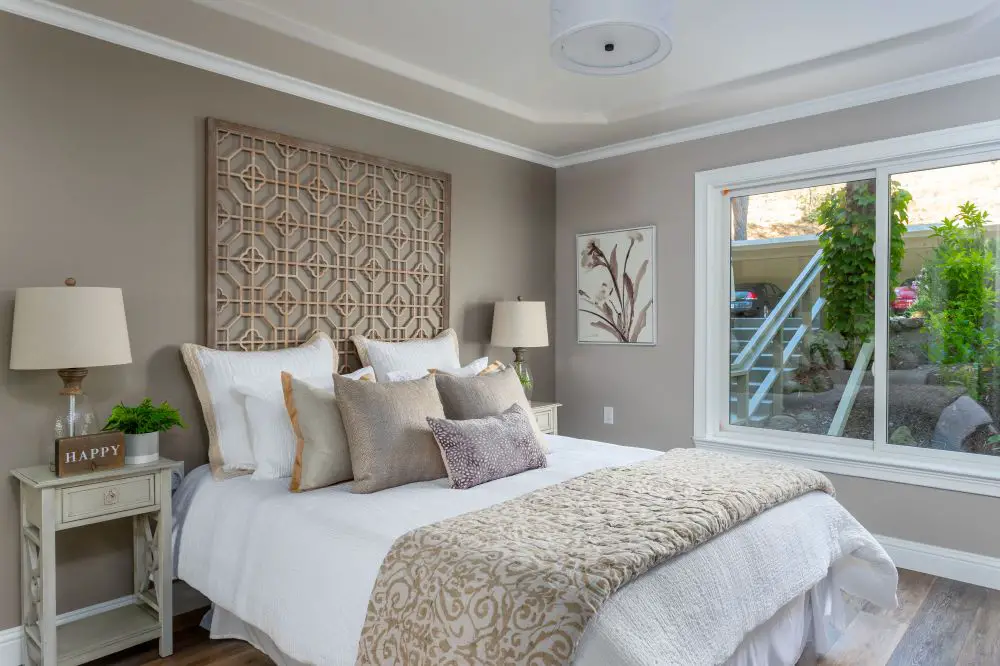 Danville bedroom with warm taupe paint walls, neutral bedding, wood wall art, and soft natural light