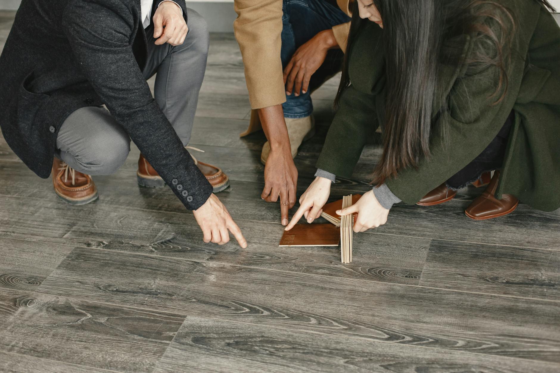 Homeowners comparing gray wood flooring samples on installed plank floor during home remodel