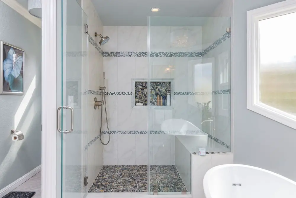 Custom glass shower with pebble tile floor and freestanding tub in bathroom remodel