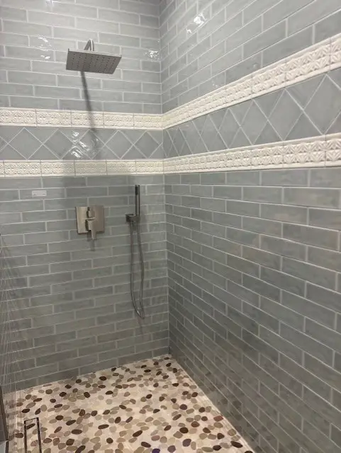 Walk-in shower with gray subway tiles and pebble stone floor.