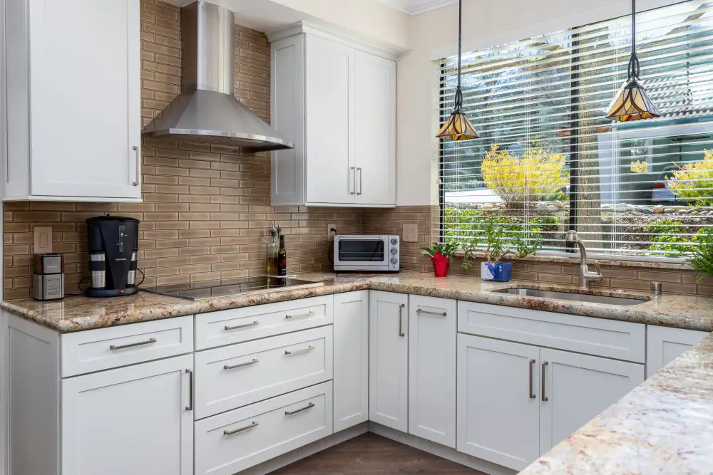 Kitchen corner with sink under window, white cabinets, and granite countertops