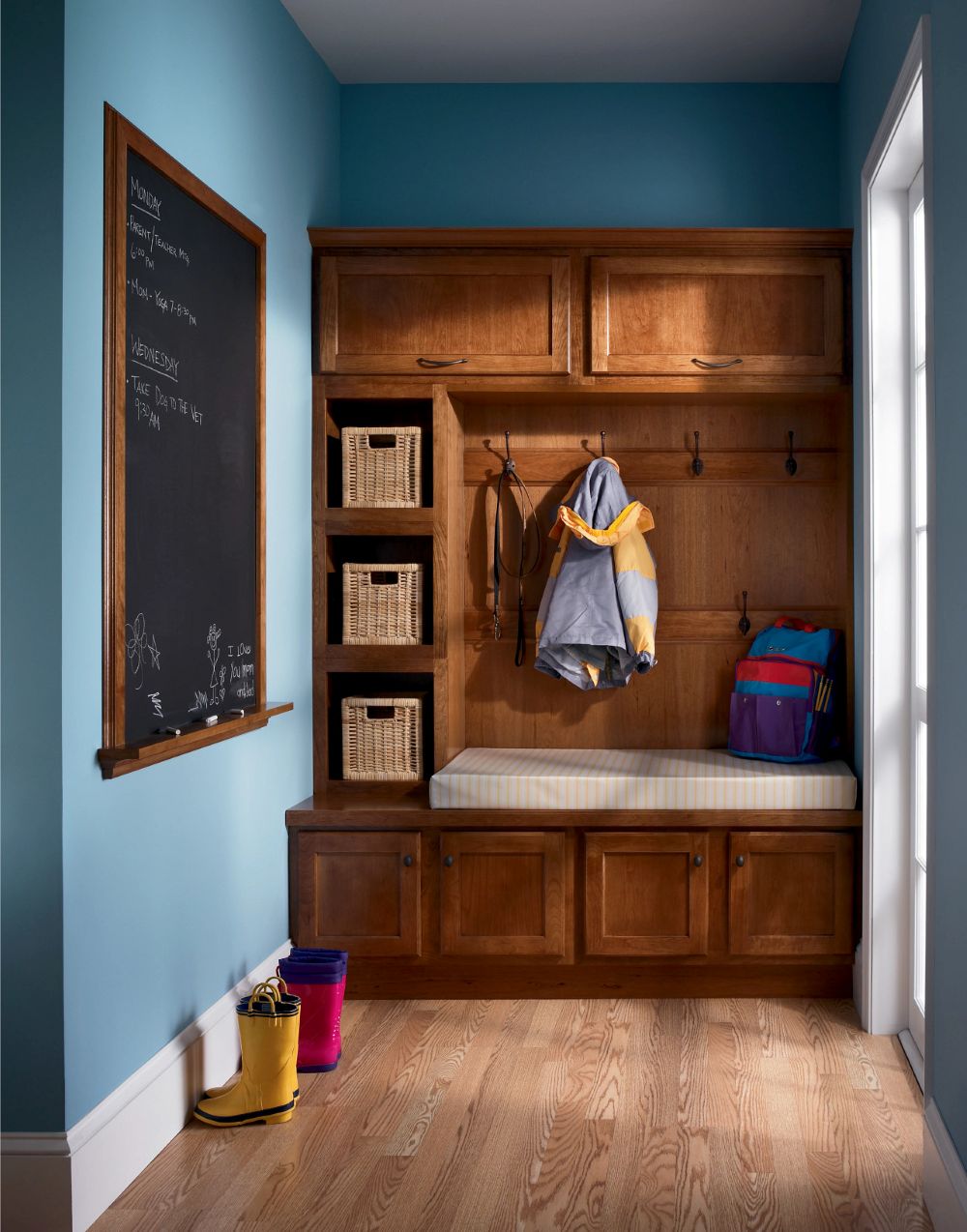 Warm wood KraftMaid mudroom with bench seating, storage cubbies, and wall hooks for family organization