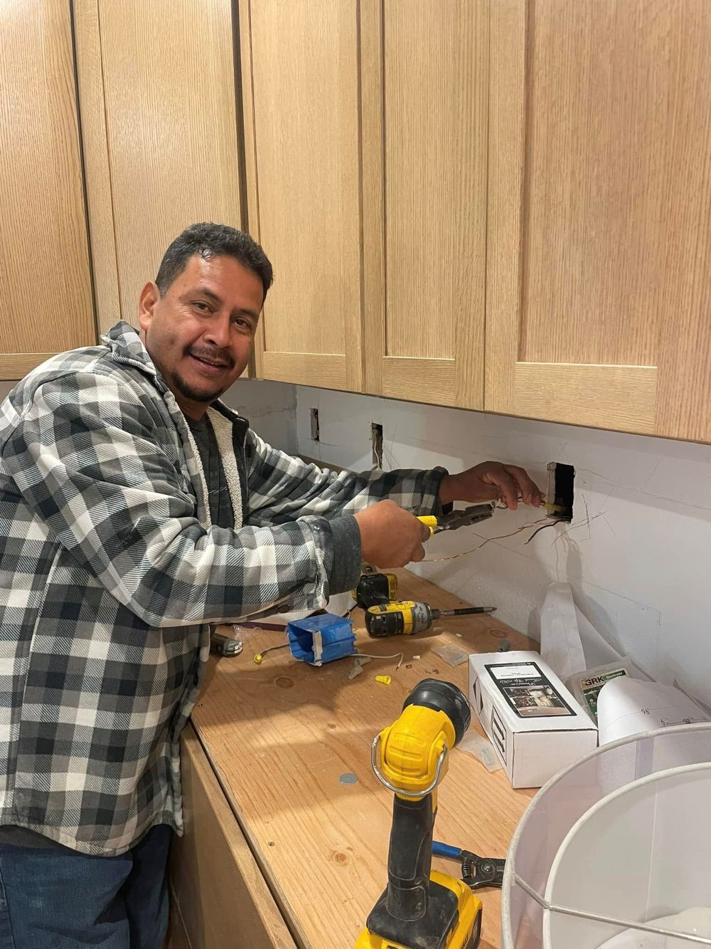Licensed electrician installing electrical wiring and outlet boxes beneath custom wood kitchen cabinets during a kitchen remodel in the East Bay.