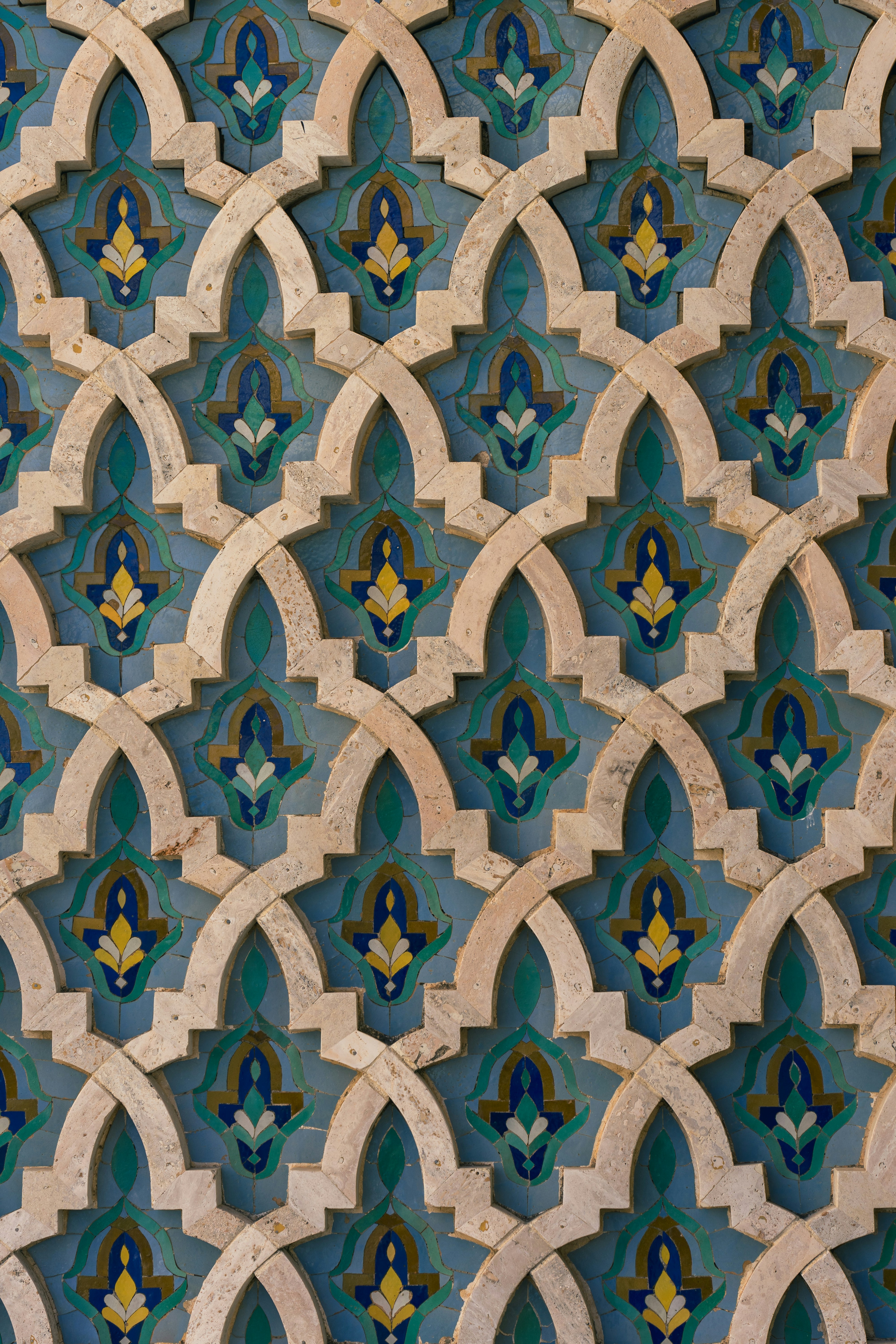 Close-up of Moroccan zellige wall tiles in blue and green tones with beige arabesque frames and intricate floral geometry.