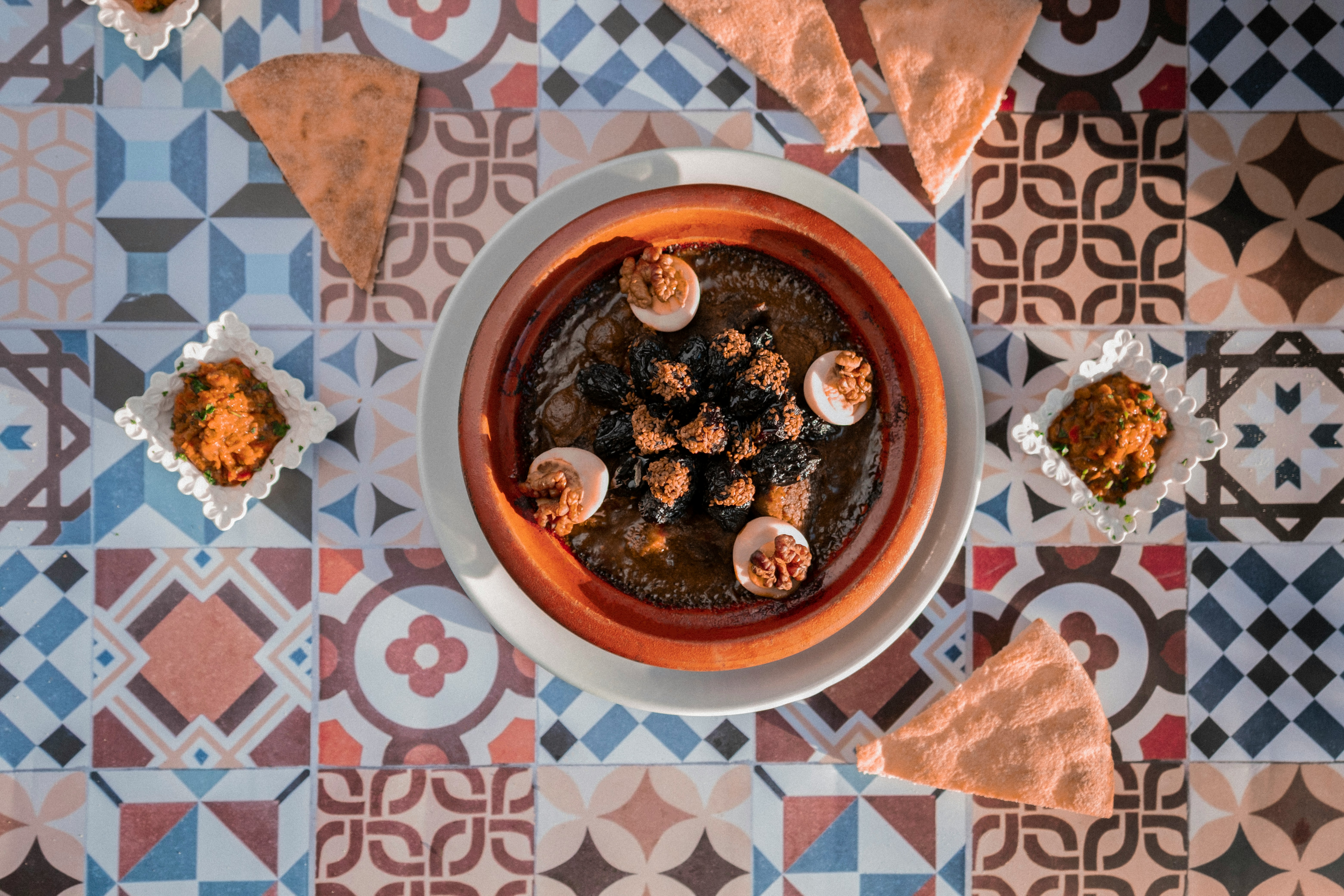 Colorful Moroccan patterned cement tiles used as a table surface, with a traditional tagine and small side dishes on top.