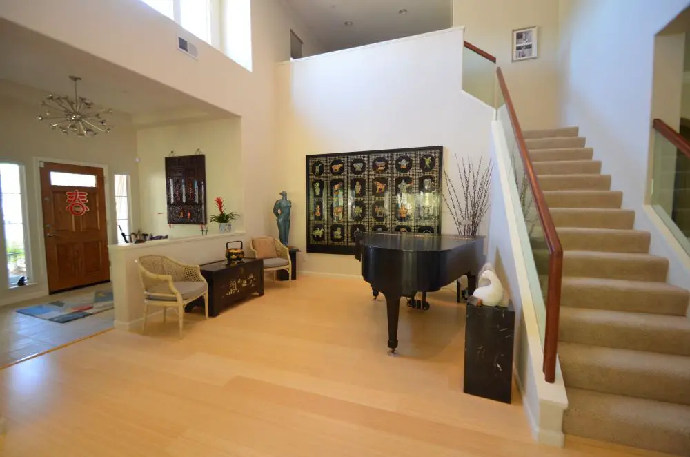Open entry with staircase, high ceilings, hardwood floors, and piano seating area
