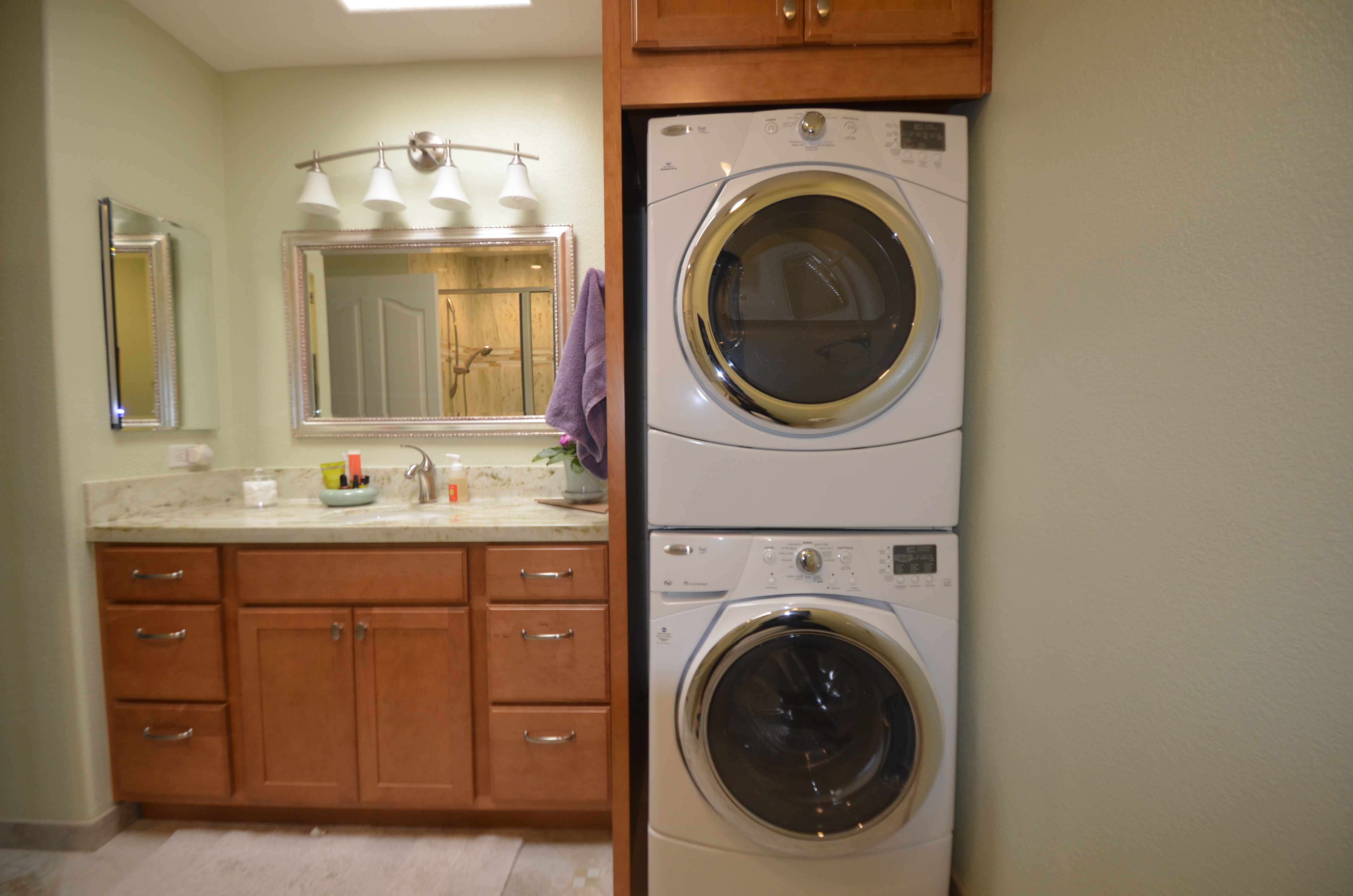 Side by side washer and dryer in Pleasant Hill CA laundry room with white cabinets storage and natural light