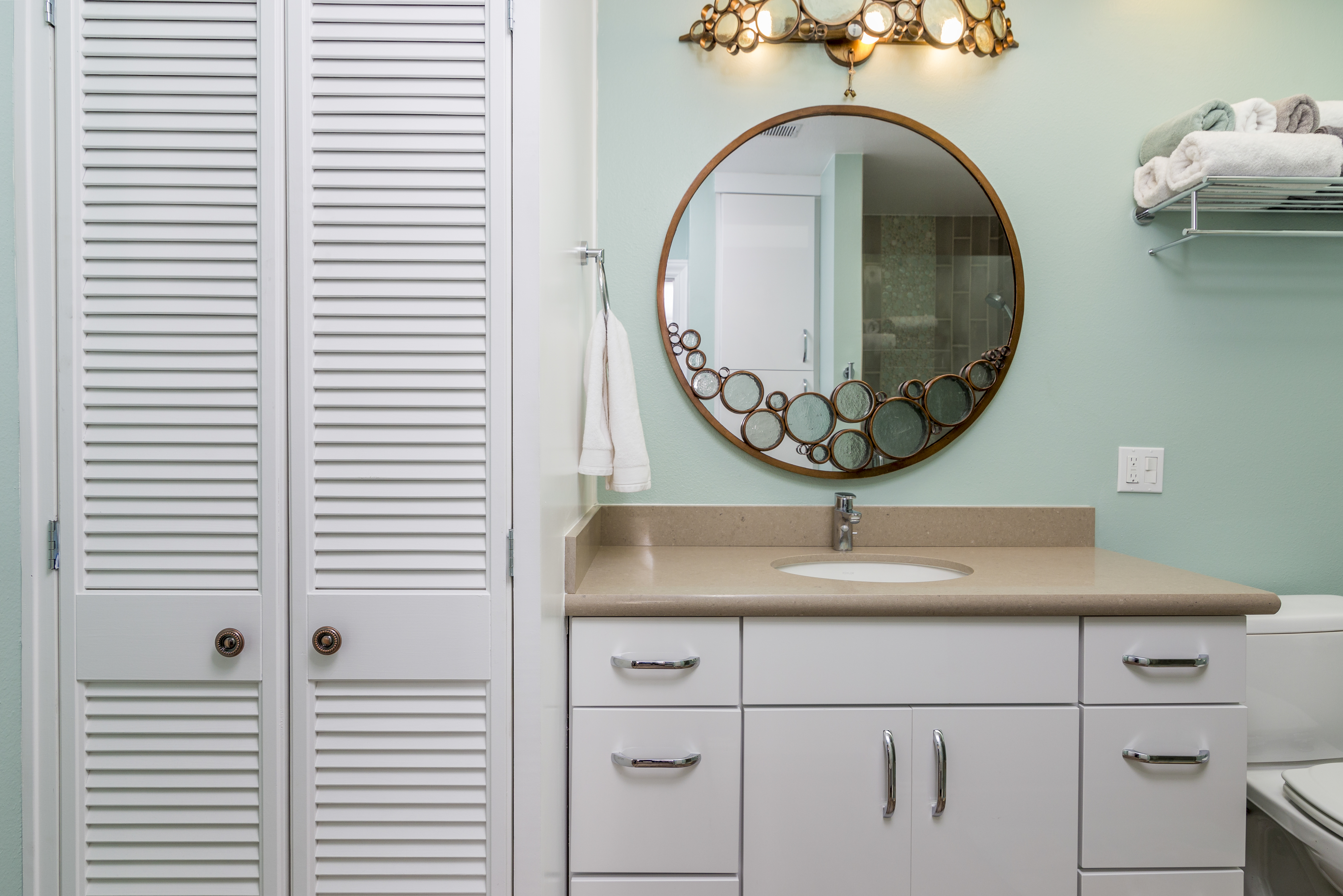 Round bathroom mirror on soft green wall above white vanity with simple design